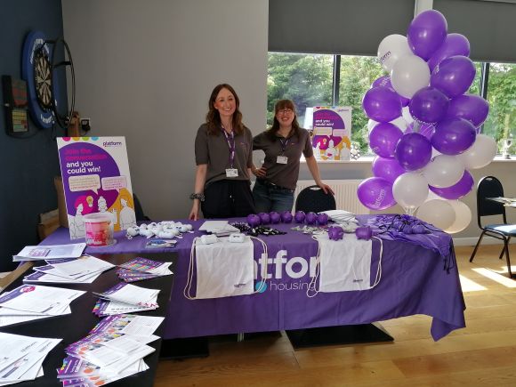 Two Platform colleagues are pictured smiling behind their Community Roadshow desk