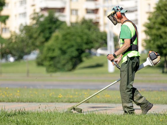 Male with high-vis clothing, face guard and safety equipment strimming a grassed area on an estate