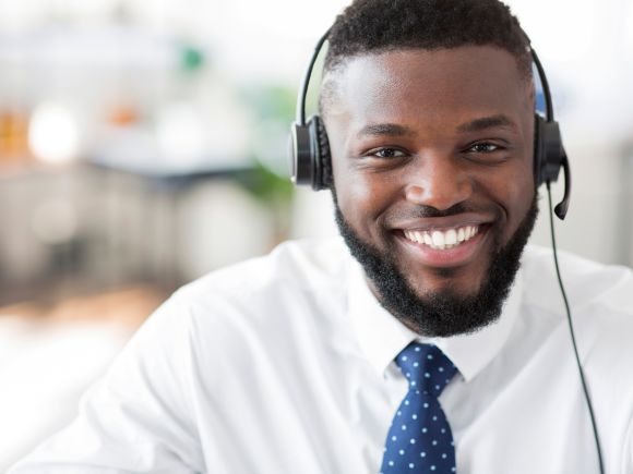 Young male customer services advisor smiling and speaking to a customer through his headphones
