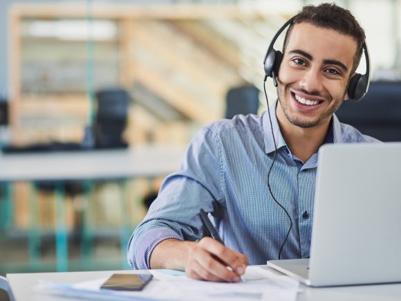 Service operative at a laptop smiling and taking notes from a call