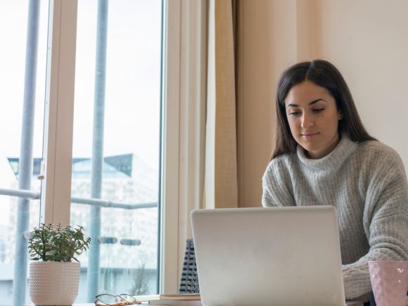 Woman working on a laptop at home in front of a window