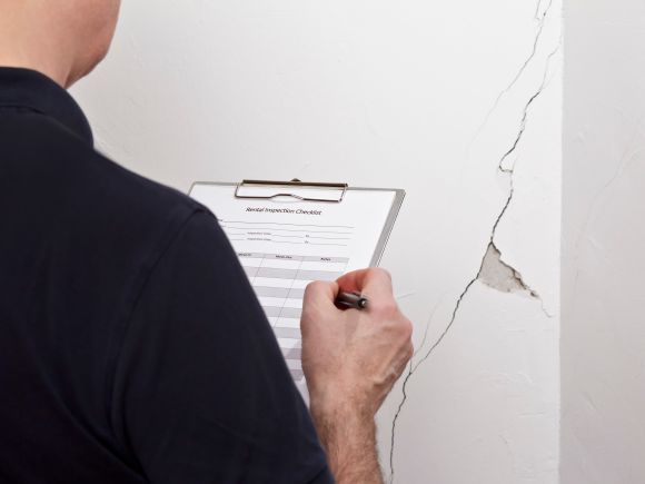 Officer inspecting a home before moving out - viewing a crack in the wall and noting against a checklist.