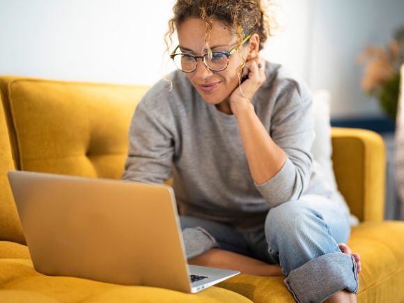 Woman sat on a yellow sofa looking at her laptop