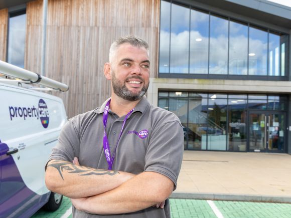 Colleague in a Platform Property Care polo shirt stands with arms folded beside a branded van, outside a modern office building.