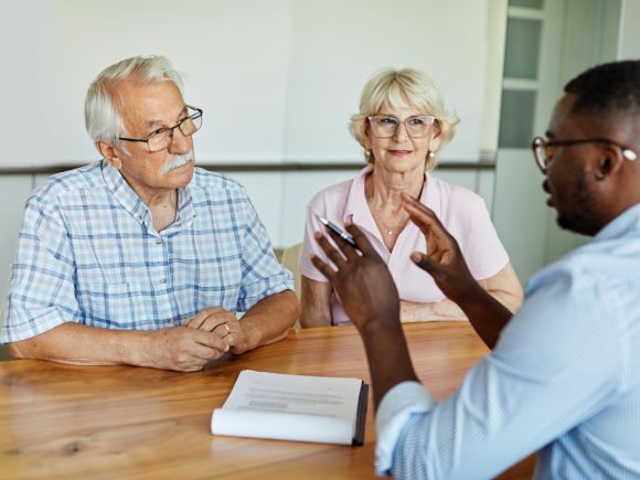 Older couple talking and receiving help and support from an advisor sat around a table