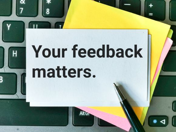 Blue note with the words Your Feedback Matters in black, against more post it notes and a key board
