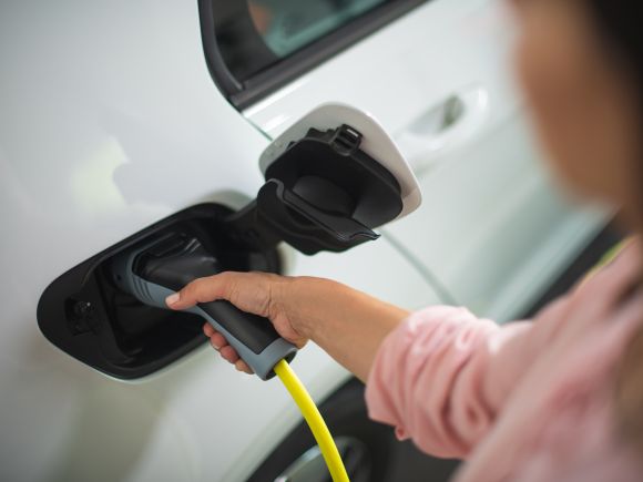 Lady in pink shirt inserting a charger into her electric white car