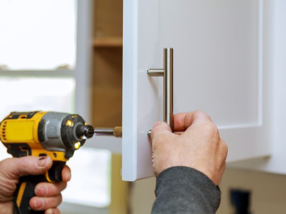 Person using a electric screwdriving to fit a handle to a cupboard