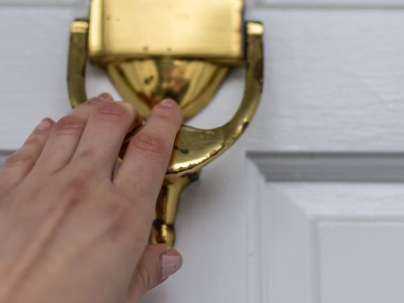 Let us in - hand knocking on a brass door knocker