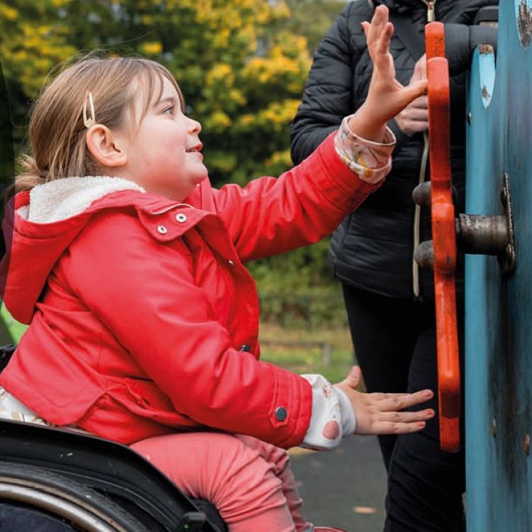 Young girl in a wheelchair playing at the park with her Mom