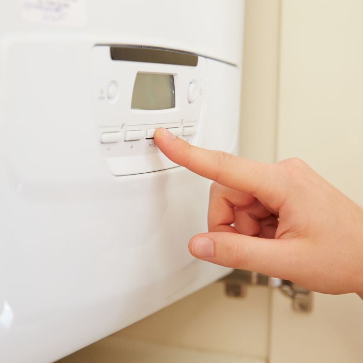 A hand pressing a button on a domestic boiler