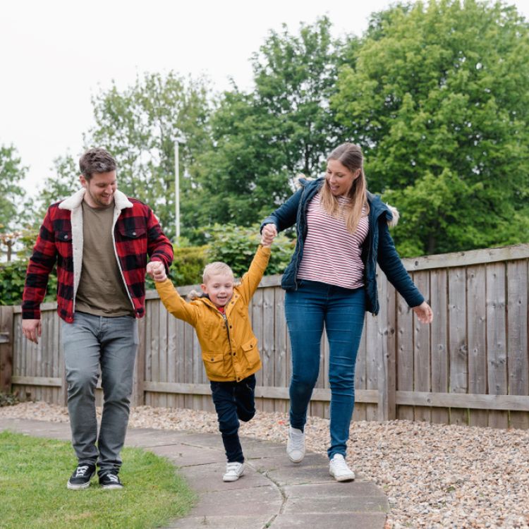 Little boy holding his parents hands as they walk along the garden path to get back to the house. They are smiling and laughing on the way back