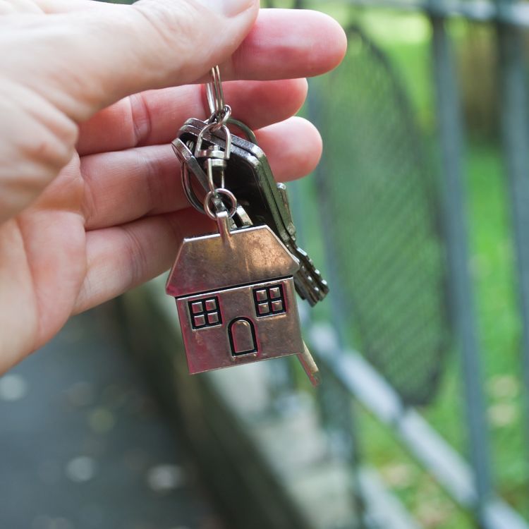 closeup of man giving metallic key with house shaped key chain to lodger