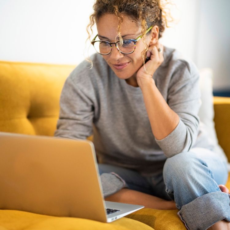 Woman sat on a yellow sofa looking at her laptop