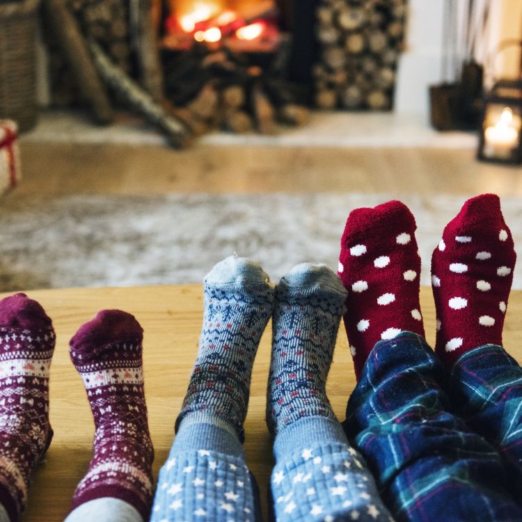 Image of family feet in thick socks resting on a table in front of a fire as they are all prepared for winter
