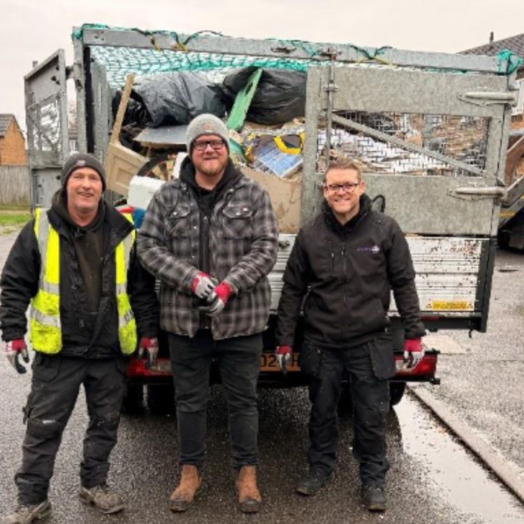 Three workers in outdoor workwear and gloves stand in front of a waste collection truck filled with rubbish on a residential street, taking part in a community clean-up in Sutton on Sea.