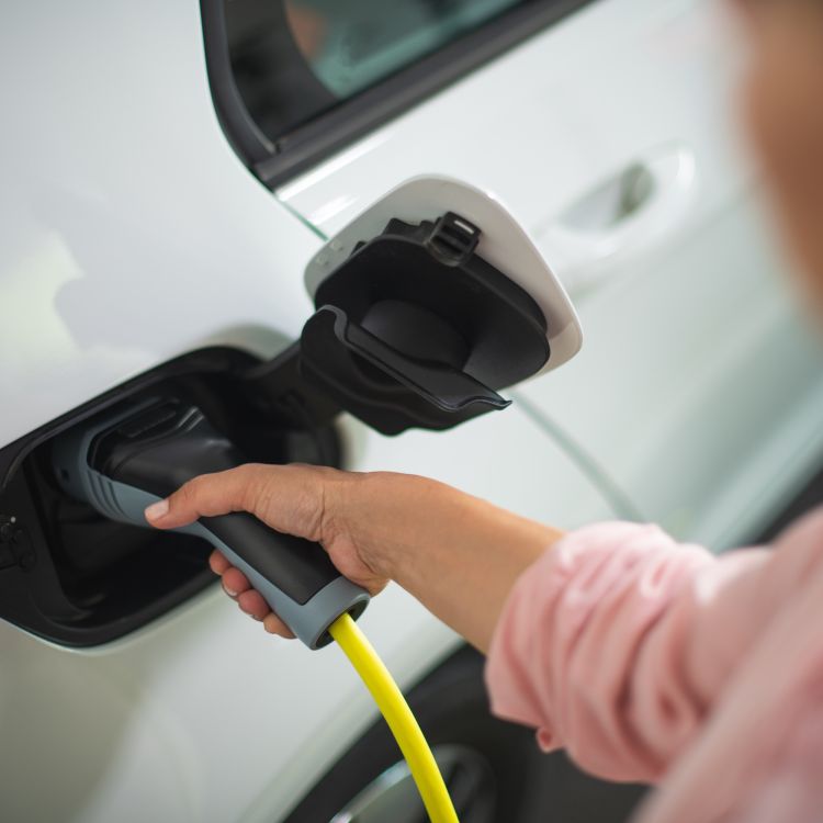Lady in pink shirt inserting a charger into her electric white car