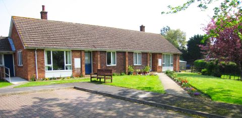 A row of red-brick bungalows with small front gardens, flowers, and a shared paved area.