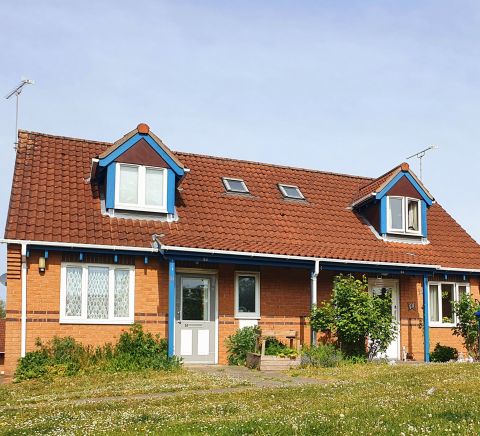 A pair of red-brick houses with blue trim and front gardens, viewed from a grassy area.