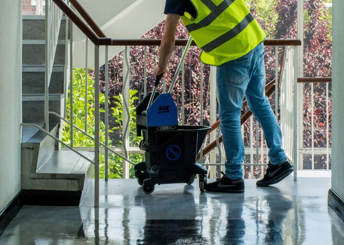 Male in a high-vis vest mopping a staircase floor