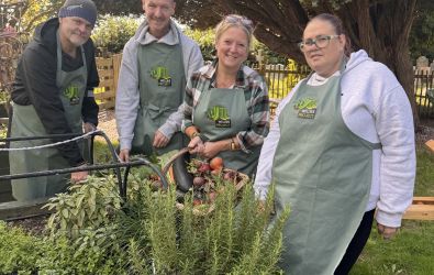 Participants of the WELLIES project, in a garden wearing WELLIES PROJECT branded aprons and holding a basket of mixed vegetables